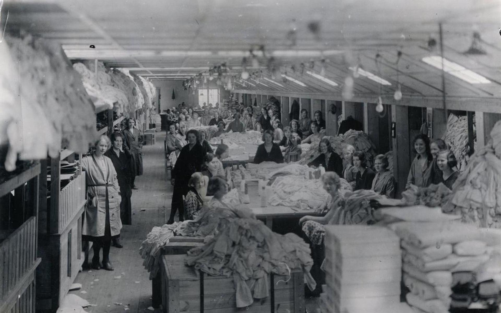 Kvinnliga fabriksarbetare står uppställda för fotografering i fabrikslokal på &quot;Strumpan&quot; (Viktor Samuelsons fabrik), okänt årtal.