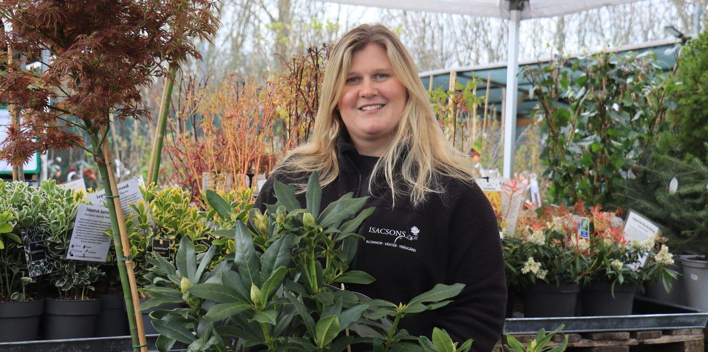 En tjej står omgiven av växter. 