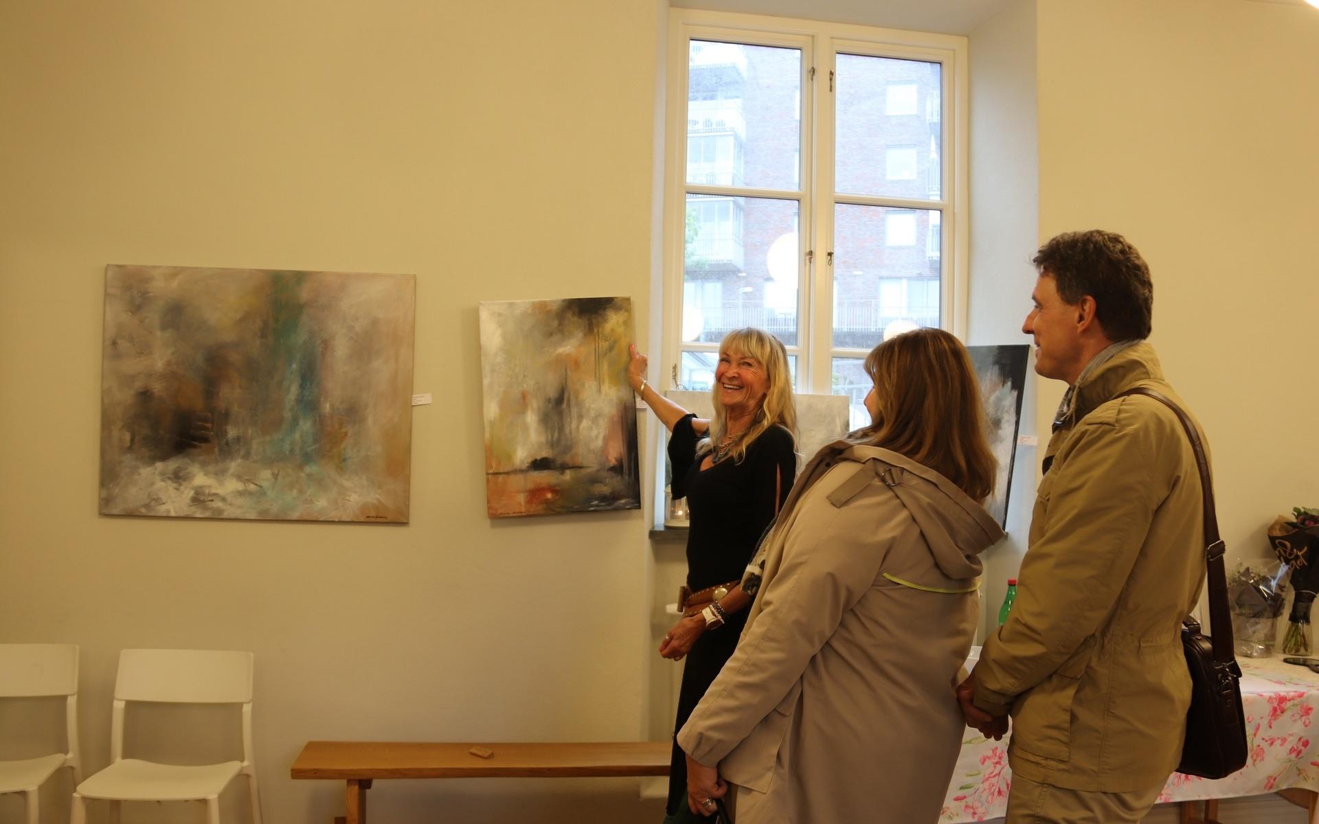 Gunilla Heidenberg håller upp en av de akrylmålningar som gick att titta på i Götiska huset vid Mölndals kråka.